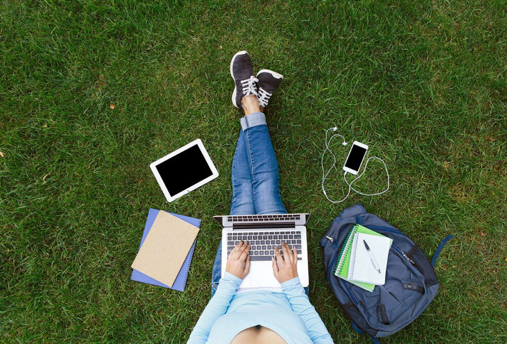 Female+student+sitting+on+grass+surrounded+by+notebook,+iphone,+backpack